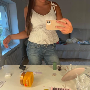 Vit ribbad linnetopp med spetsdetaljer - Säljer en superfin vit linnetopp med ribbad struktur och spetsdetaljer i midjan och nedtill. Toppen har smala axelband med knyt och en v-ringad hals. Perfekt för varma dagar och ger en fräsch och söt look.