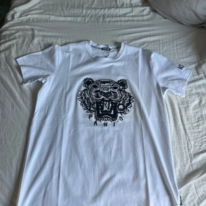 Vit Kenzo t-shirt med tigertryck - Kenzo t-shirt i vitt med ikoniskt svart broderat tigerhuvud och logga på bröstet. Kortärmad modell med rund hals och Kenzo-broderi på ärmen. Tillverkad i mjuk bomull för skön passform. Perfekt statement-plagg för dig som gillar streetstyle och designer. OBS HELT NY, pris kan diskuteras