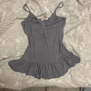 Topp - Säljer en grå tunika från Vyrus i mjukt bomullsmaterial. Klänningen har smala axelband, volangkant nedtill och en snygg rynkning framtill. Perfekt för dig som gillar enkel och chill stil med lite extra detalj i nederdelen. Det står xl på lappen men skulle säga M.
