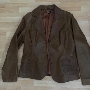 Brun skinnkavaj från Sorbet som ny.XL - Snygg brun kavaj i skinn från Sorbet i storlek XL. Klassisk modell med breda slag, tre knappar framtill och två fickor med lock. Perfekt för dig som vill ha en stilren och tidlös jacka med cool vintagekänsla. Storlek är förminskad och är som M, bröst 100cm. Använd en gång.