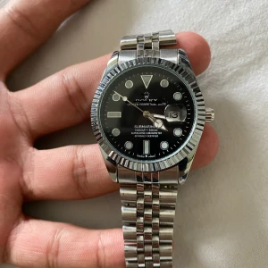 stilren klocka silver(R€P) - Snygg klocka i silverfärgat rostfritt stål med svart urtavla och datumfönster. Klassisk rund form, räfflad bezel och länkarmband. Perfekt accessoar för dig som gillar stilrena detaljer.