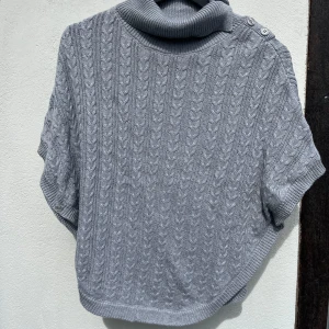 Grå stickad pullover Hampton Republic - Säljer en grå stickad pullover tröja från Hampton Republic, utan ärmar, med snygg kabelstickad struktur. En nedvikbar polokrage och två knappar på axeln o en på halsen som gör att man kan förstora kragen. I nyskick, hel o ren. Storlek 146/152. Gjord av bomull.