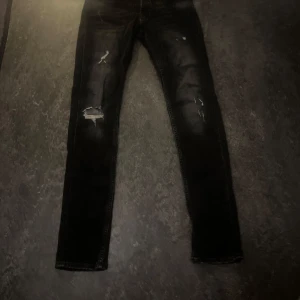 Svarta skinny jeans med slitningar - Svarta jeans med skinny passform och coola slitningar på båda benen. Jeansen har en mörk tvätt och är tillverkade i klassiskt denimtyg. Perfekta för dig som gillar en edgy streetstil.