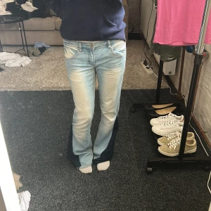 Ljusblåa Bootcut jeans - Säljer ett par ljusblå bootcut jeans med coola mörkblå paneler längs utsidan av benen. Jeansen har klassiska fem fickor, snygga slitningar och broderad detalj på bakfickorna. Perfekt för dig som gillar retrovibbar och unik stil. Jeansen har varit straight men själv så har jag gjort dom till bootcut, jeansen är uppsydda några cm men passar mej som är runt 165-170. Lite små detaljer syns på det sydda men inget som märks när det är på utan bara när man kollar noga!