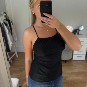 Svart topp - Svart topp med tunna axelband och ribbad struktur. Toppen är från Gina Tricot i storlek xs. Kan stylas på olika sätt. 