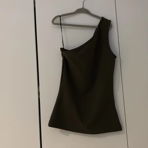 Mörkgrön oneshoulder topp från H&M - Snygg mörkgrön topp från H&M i oneshoulder-modell med ett smalt axelband på ena sidan. Toppens stilrena design gör den enkel att matcha med olika outfits. Materialet känns mjukt och har en lätt stretch för skön passform.