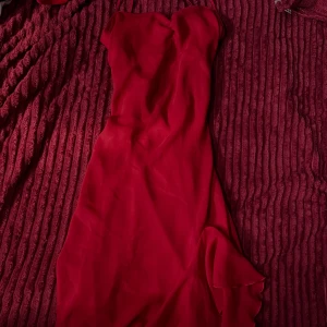 Röd långklänning med smala axelband - Säljer en elegant röd långklänning med smala axelband och figurnära passform. Klänningen har ett jack och slike under samt  en mjuk, flytande siluett och är tillverkad i ett tunt, lätt material som ger ett snyggt fall. Perfekt för dig som vill sticka ut med en klassisk look.💋💋💋