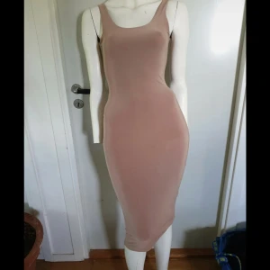 Beige tight långklänning med öppen rygg - Snygg beige långklänning i stretchigt syntetmaterial med figurnära passform. Klänningen har smala axelband, rundad halsringning och en djup öppen rygg. Notera bild 5 