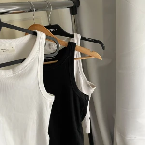 Svart och vit ribbad linnetopp Gina Tricot - Två stilrena ribbade linnetoppar från Gina Tricot i svart och vitt. Modellen är klassisk med rundad hals och breda axelband, perfekt att matcha med jeans eller shorts. Materialet är mjuk bomull som känns skönt mot huden. Säljes tillsammans!