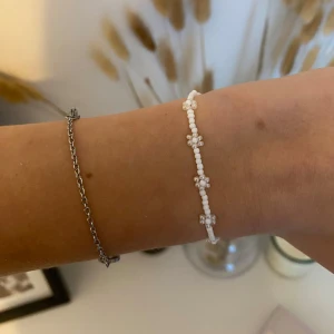 Pärlarmband med blommor i vitt - Supergulligt minimalistiskt egentillverkat armband med små vita pärlor och blommor av pärlor längs hela bandet. Armbandet har en silverfärgad kedja och lås för justering🤍