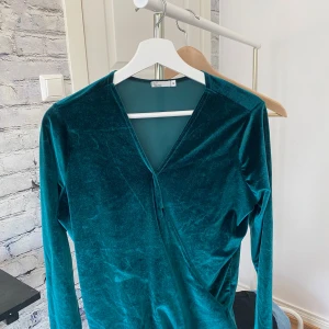 Petrolgrön omlottopp i sammet NLY Trend - Snygg petrolgrön omlottopp från NLY Trend i mjuk sammet. Toppen har v-ringad hals och långa ärmar. Passformen är normal och materialet känns riktigt skönt mot huden.