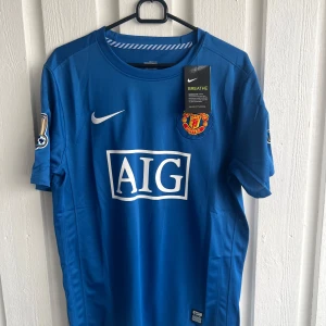 Blå Manchester United Ronaldo 7 tröja - Snygg blå Manchester United fotbollströja från Nike med AIG som sponsor på bröstet och Ronaldo 7 tryckt på ryggen. Kortärmad modell med Premier League-patch på ärmen och klubbmärke på framsidan. Tillverkad i lätt och ventilerande material.