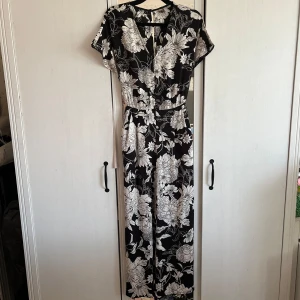 Svart blommig byxdress - En svart byxdress med vita blommor i storlek 36 från H&M. Dressen har korta ärmar, v-ringning och vida ben samt knäppning baktill vid nacken. Fickor på sidorna samt tillhörande bälte som är avtagbart!💞