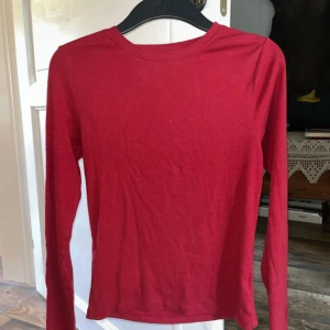 Röd långärmad basictröja C 170 - Enkel och stilren röd långärmad tröja från Cubus i storlek 170. Tröjan har rund halsringning och är gjord i mjuk bomull, perfekt att matcha med jeans eller kjol. Snygg att bära som den är eller under en jacka.