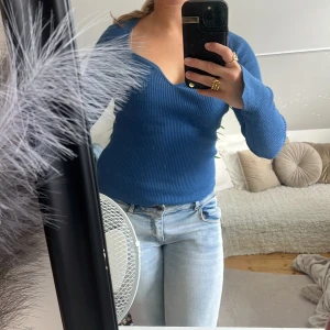 Blå ribbad stickad tröja med v-ringning - Säljer en blå ribbad stickad tröja med snygg v-ringning och lång ärm. Tröjan har en figurnära passform och är perfekt för dig som gillar en enkel men stilren look. Passar till både jeans och kjol för en chill vibe.