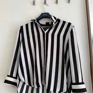 Svartvit randig skjorta Gina Tricot - Snygg skjorta från Gina Tricot i storlek 38 med breda svarta och vita ränder. Skjortan har klassisk krage, knäppning framtill och långa ärmar med randiga manschetter. Har en liten fläck (borde gå bort i tvätten) 