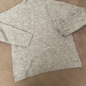 Grå ribbad polotröja - Mysig grå ribbad polotröja med lång ärm och hög hals. Perfekt för lager-på-lager och chill dagar. Tröjan har en relaxed fit och är stickad i ett mjukt material som håller dig varm under kyliga dagar.