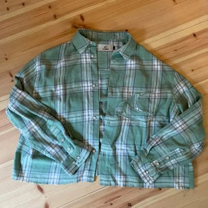 Grön rutig skjorta från Scuffers - Grön och vit rutig skjorta från Scuffers med klassisk krage och långa ärmar. Skjortan har knäppning framtill och en broderad logga på bröstet. Perfekt för en avslappnad och cool stil.