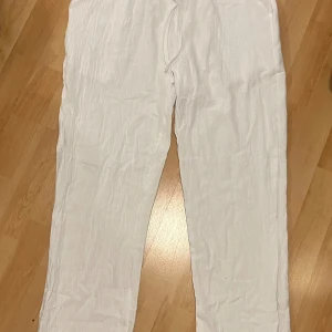 Vita linnebyxor  - Snygga och luftiga vita linnebyxor med avslappnad passform och snörning i midjan. Perfekta för varma dagar när du vill ha en chill och stilren look. Lätta att matcha med både t-shirt och skjorta.