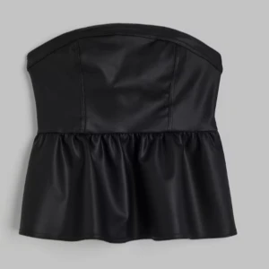 Svart tubtopp i skinnimitation - Säljer en supersnygg svart axelbandslös tubtopp i skinnimitation med peplum. Prislapp kvar! Helt slutsåld💗