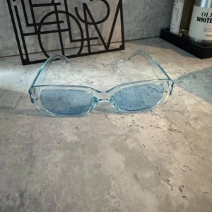 Isblå transparenta solglasögon - Snygga rektangulära solglasögon med transparent isblå båge och matchande blåtonade glas. Glasögonen har en modern vibe och passar perfekt för dig som vill sticka ut med en cool accessoar. Lätta och bekväma att bära hela dagen.