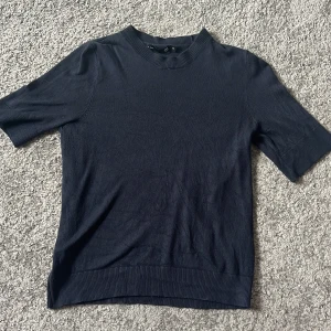 Mörkblå stickad tröja 157 XS - En stilren mörkblå stickad tröja från 157 i storlek XS. Tröjan har korta ärmar, ribbade muddar vid hals, ärmslut och nederkant. Perfekt för dig som gillar en enkel och clean look med en bekväm passform.