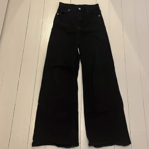 Svarta wide jeans från H&M Divided - Jättesnygga svarta jeans från H&M Divided i storlek 34. Modellen har hög midja och vida ben för en trendig och avslappnad look. Har extremt fin passform. Klassisk femficksdesign och knappgylf. Perfekta till sneakers eller boots. 