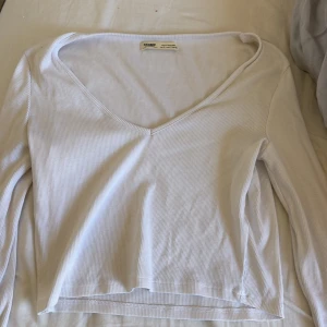 Vit ribbad långärmad tröja från pull and bear  - Säljer en stilren vit långärmad tröja från Filippa K. Tröjan är ribbad med v-ringad hals och har en mjuk, stretchig känsla. Perfekt för lager-på-lager eller som den är till jeans eller kjol.