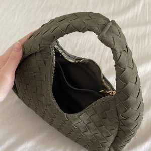 Olivgrön flätad liten väska. - Snygg olivgrön väska med flätad design och rundad form. Lyxig känsla och perfekt för dig som vill ha en stilren detalj till din outfit.