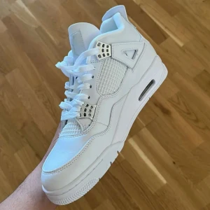Jordan 4 Pure Money  - Nike Air Jordan 4 sneakers i helvitt skinn med vita meshpaneler och silvriga detaljer vid snörningen. Klassisk chunky sula med synligt luftfönster och rund tå. Perfekta för dig som vill sticka ut med en clean och sportig look.
