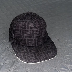 Fendi keps - Snygg svart keps från Fendi med ikoniskt FF-logomönster över hela kepsen. Kepsen har böjd skärm med vit kant och justerbar rem baktill. Tillverkad i polyester och bomull för en bekväm och stilren look.