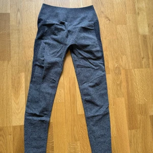 Mörkgrå tränings tights med hög midja - Snygga mörkgrå tränings tights med hög midja, scrunch och tight passform. Perfekta för träning eller chill, i mjukt och stretchigt material som sitter skönt hela dagen. Enkla att matcha med både oversized hoodies och crop tops.