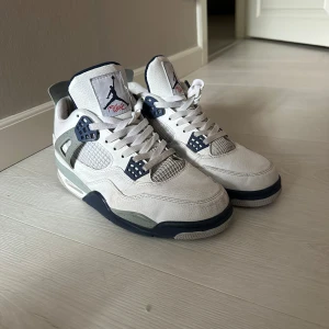 Nike Air Jordan 4 Retro White/Navy - Box tillkommer! Säljer ett par Nike Air Jordan 4 Retro i vitt skinn med detaljer i marinblått och grått. Skorna har meshpaneler, klassisk snörning och Jumpman-logga på plösen och hälen. Sulan är vit med inslag av blått och rött. Perfekta för dig som gillar ikoniska sneakers med streetkänsla.