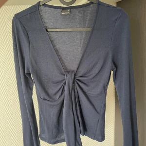 Mörkblå topp från Gina Tricot - Snygg mörkblå topp från Gina Tricot med lång ärm och djup v-ringning. Toppen har knyt framtill. Tillverkad i mjuk bomullsmix som känns skön mot huden. 