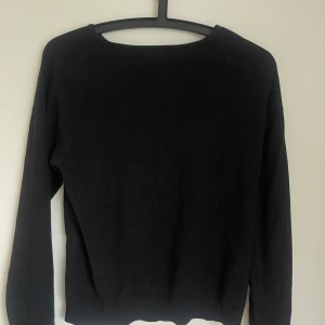 Svart stickad tröja XOXO Friends - Enkel svart stickad tröja från XOXO Friends med rund halsringning och långa ärmar. Tröjan har en liten slits i nederkanten på sidorna för en snygg detalj. Perfekt till jeans eller kjol för en clean look. Passar S.