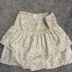 Prickig volangkjol från Zara - Supersöt kort kjol från Zara i beige med svarta prickar. Kjolen har smock i midjan och dubbla volanger.
