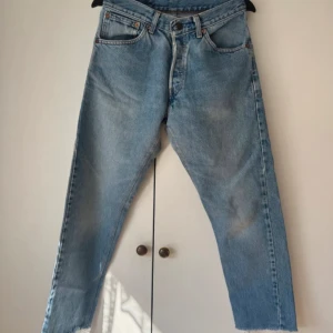 Levi's 501 ljusblå jeans straight fit - Klassiska Levi's 501 jeans i ljusblå tvätt med raka ben och femficksmodell. Jeansen har hög midja, knappgylf och råa benslut för en avslappnad vibe. Perfekta till sneakers eller boots och funkar året runt. Ikonisk röd Levi's-tag på bakfickan.