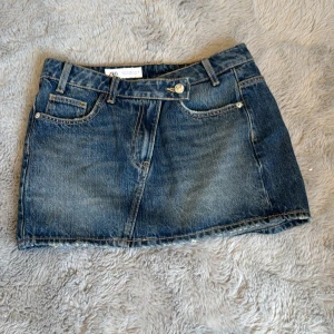 Blå jeanskjol från Zara - Snygg blå jeanskjol från zara med klassisk femficksdesign, bälteshällor och knappstängning framtill. Kjolen är kort 