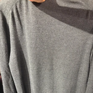 Grå polotröja Polo Ralph Lauren merinoull - Mörkgrå polotröja från Polo Ralph Lauren i mjuk och tvättbar merinoull. Klassisk design med lång ärm, ribbade muddar och diskret broderad logga på bröstet. Perfekt för dig som gillar stilrena och tidlösa plagg.