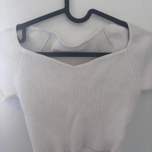 Vit ribbad topp med v-ringning - Superfin vit ribbad topp med v-ringad hals och korta ärmar. Snygg passform som framhäver axlarna och ger en fräsch look. Perfekt att matcha med jeans eller kjol för en clean stil.