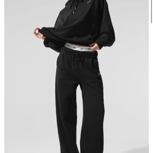 Svarta mjukisbyxor från Alo - Säljer ett par svarta mjukisbyxor från Alo med dragsko i midjan och broderad logga på höften. Byxorna har en relaxed passform och raka ben, perfekta för en chill stil.