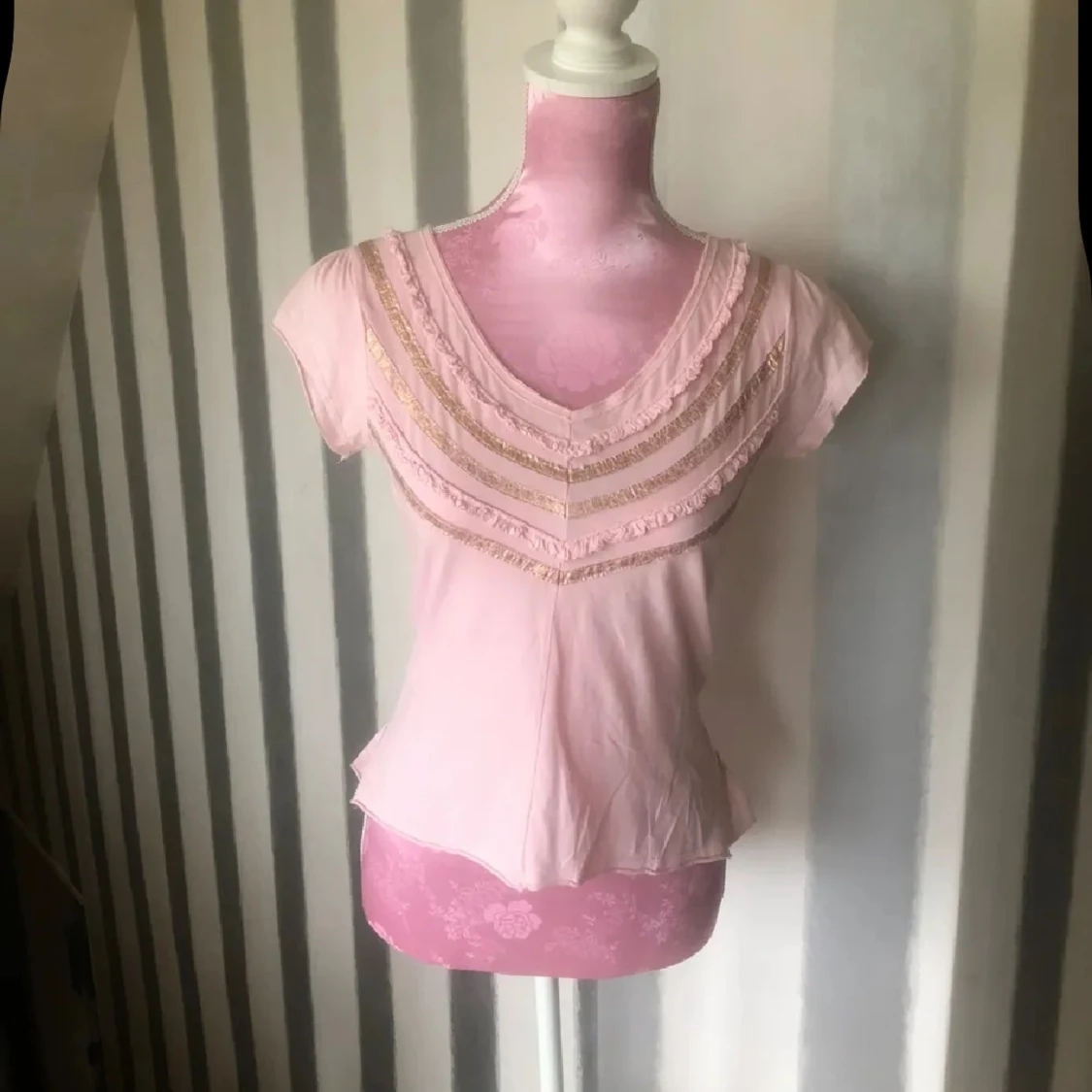 Ljusrosa blus med volang och guldiga detaljer