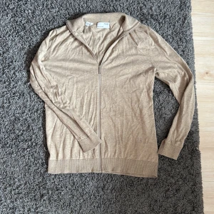 Beige ziptröja med krage - Säljer en beige ziptröja från Selected Homme. Tröjan har lång ärm, hög krage och dragkedja framtill. Tillverkad i tunn bomullsmix, perfekt för lager-på-lager. Enkel och stilren design som passar till mycket.