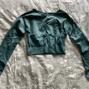 Grön croppad långärmad tröja från ICANIWILL - Säljer en grön croppad långärmad träningströja från ICANIWILL. Tröjan har en tight passform och är tillverkad i ett stretchigt syntetmaterial, perfekt för träning. Diskret logga på bröstet.