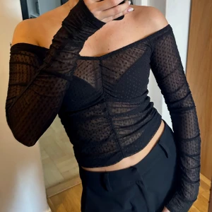 Svart mesh offshoulder topp - Svart meshtopp med prickar och offshoulder-design med långa ärmar. Toppen är genomskinlig med prickigt mönster och har en figurnära passform. Perfekt för att skapa en snygg och edgy look. Väldigt bekväm, men kommer tyvärr inte till andvändning hos mig! 