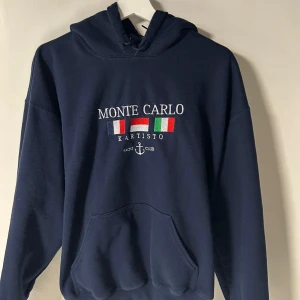 MONTE CARLO HOODIE från KARTISTO - Mörkblå hoodie från Kartisto med broderad text 'Monte Carlo' och flaggor på bröstet. Riktigt fet tröja och den passar till allt. STORLEK L MEN SITTER SOM EN M.  Riktigt fin hoodie och hör av dig vid frågor. MVH VIGGO.
