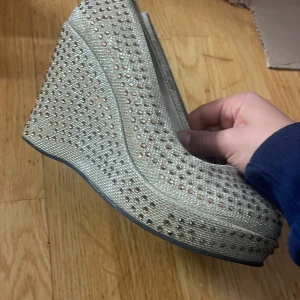 Glittriga kilklackar i guld - Säljer ett par glittriga kilklackar i guld med täckt tå och massor av små paljetter över hela skon. Perfekta för att sticka ut och ge extra höjd. Skorna har rund tå och plattformsula för extra komfort.