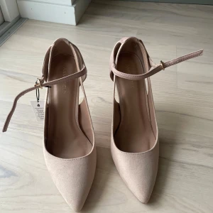 Ljusrosa pumps med ankelrem från Anna Field - Säljer ett par eleganta beige pumps från Anna Field med spetsig tå och smal klack. Skorna har en justerbar ankelrem och är tillverkade i syntetmaterial med en matt finish. Skorna är oanvända. Upphämtning i Täby eller Ulriksdal. 