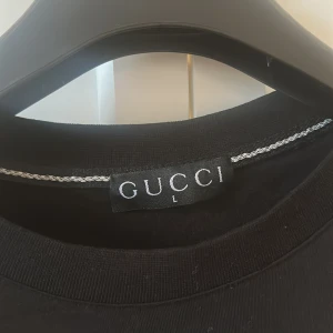 Svart t-shirt med grafiskt tryck - Säljer en svart t-shirt  i storlek L. T-shirten har ett stort grafiskt tryck framtill i vitt och rött. Klassisk rund halsringning och korta ärmar. Perfekt för dig som gillar streetwear och designerplagg.