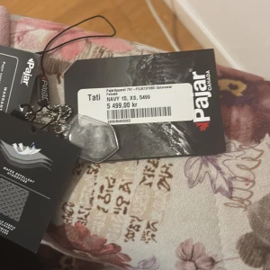 Mörkblå lång dunjacka från Pajar - Säljer en mörkblå lång dunjacka från Pajar med avtagbar huva och pälskant. Jackan har dragkedja framtill, värmande innerfoder och flera fickor. Perfekt för kalla vinterdagar. Snygg och stilren design.